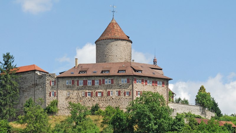 Burg Reichenberg in Oppenweiler, umgeben von grünen Bäumen und blauem Himmel. Der runde Turm und das Hauptgebäude sind aus Stein mit roten Dächern., © FVG Schwäbischer Wald