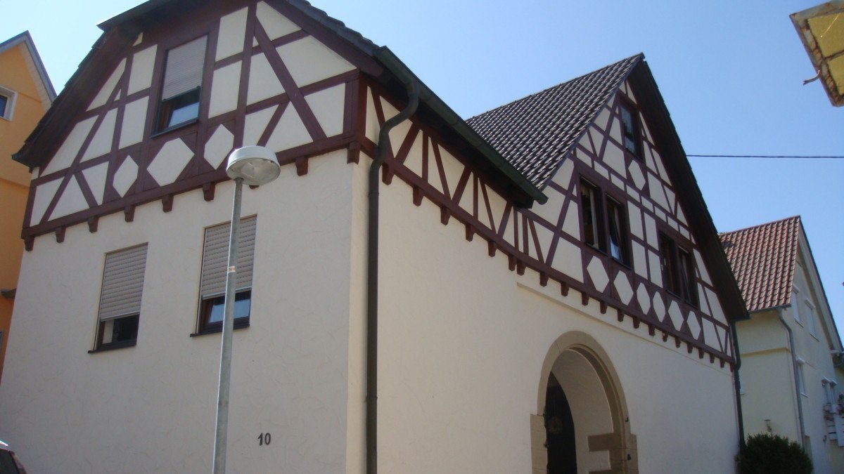 Fachwerkhaus mit weißer Fassade und braunen Balken, Satteldach und Rundbogeneingang. Eine Straßenlaterne steht davor., © Land der 1000 Hügel - Kraichgau-Stromberg