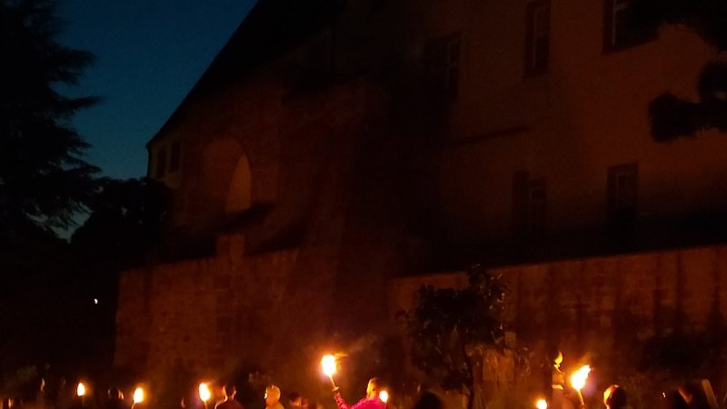 Eine Gruppe von Menschen h&auml;lt Fackeln bei Nacht vor einem historischen Geb&auml;ude. Der Himmel ist dunkelblau, und die Szene wirkt geheimnisvoll., &copy; Stadtmarketing Leonberg