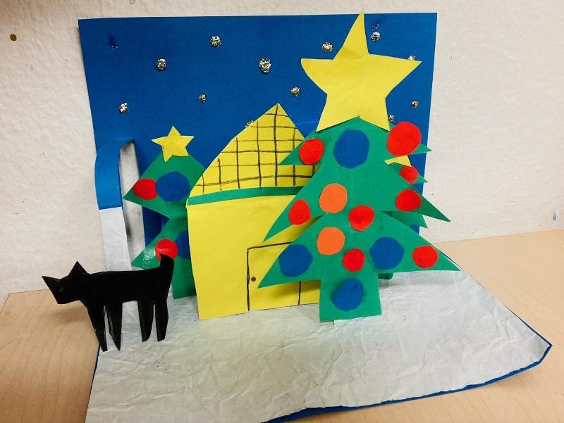 Ein buntes Pop-Up-Buch mit einem Weihnachtsbaum, einem Haus und einer schwarzen Katze aus Papier auf einem Tisch., © Kunstschule Labyrinth Ein buntes Pop-Up-Buch mit einem Weihnachtsbaum, einem Haus und einer schwarzen Katze aus Papier auf einem Tisch., © Kunstschule Labyrinth