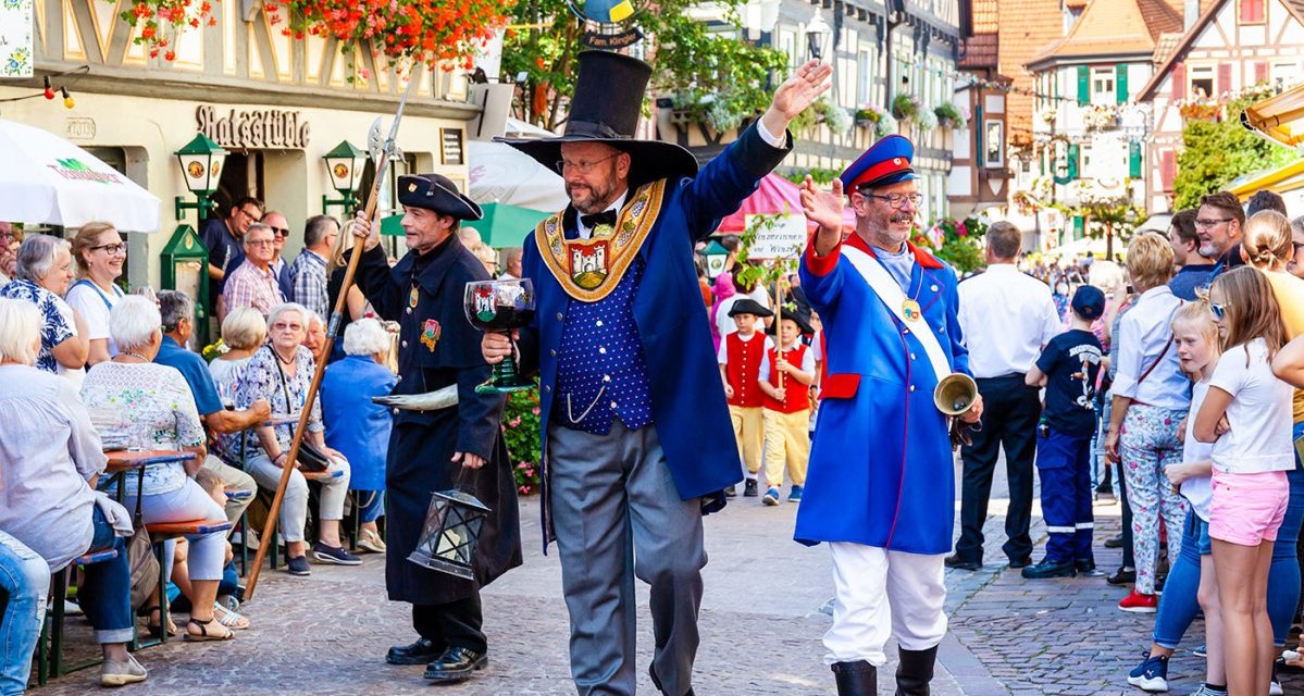 Parade beim Winzerfest in Besigheim: Menschen in historischen Kostümen marschieren durch eine belebte Straße, umgeben von Zuschauern und Fachwerkhäusern., © Stadt Besigheim Parade beim Winzerfest in Besigheim: Menschen in historischen Kostümen marschieren durch eine belebte Straße, umgeben von Zuschauern und Fachwerkhäusern., © Stadt Besigheim