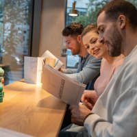 Drei Personen sitzen an einem Tisch in einem Restaurant und lesen die Speisekarte. Im Hintergrund ist ein Fenster mit Blick nach drau&szlig;en., &copy; Stuttgart-Marketing GmbH, Martina Denker