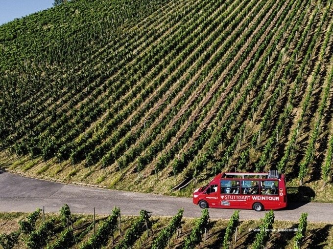 Ein roter Tourbus mit der Aufschrift 'Stuttgart Weintour' f&auml;hrt an einem Weinberg entlang., &copy; SMG, Thomas Niederm&uuml;ller
