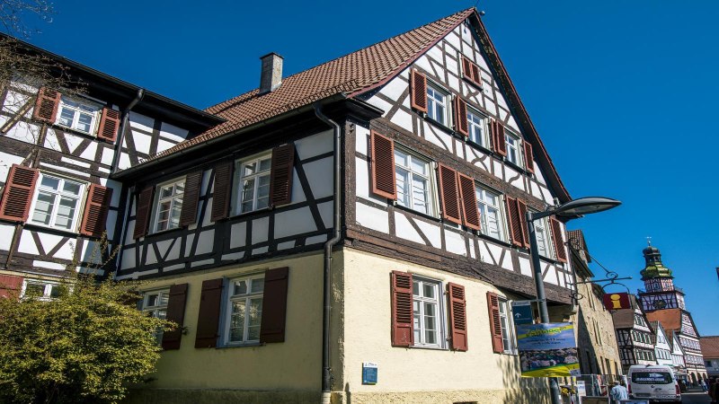 Seitliche Ansicht eines Fachwerkhauses in Kirchheim unter Teck, mit roten Fensterläden und blauem Himmel im Hintergrund., © SMG, Sarah Schmid