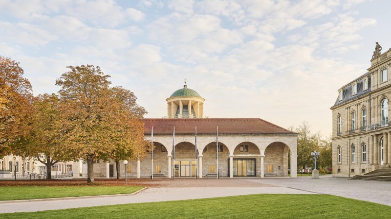 Historisches Gebäude mit Kuppel und Bögen, umgeben von herbstlichen Bäumen und gepflegtem Rasen., © Simon Sommer