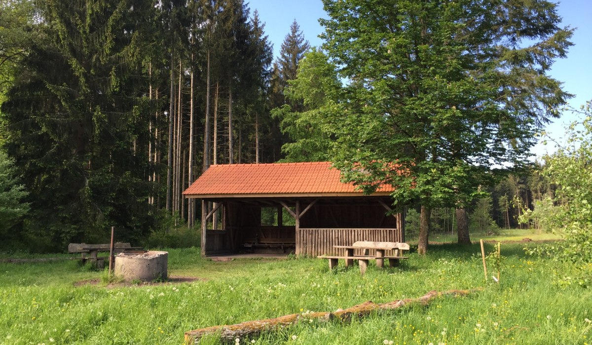 Ein Grillplatz mit Holzhütte und Picknicktisch auf einer grünen Wiese, umgeben von hohen Bäumen., © www.pro-cycl.de Ein Grillplatz mit Holzhütte und Picknicktisch auf einer grünen Wiese, umgeben von hohen Bäumen., © www.pro-cycl.de