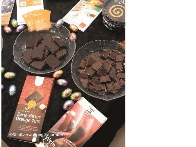 Schokoladenstücke auf Tellern, umgeben von bunten Ostereiern und Prospekten auf einem Tisch., © Eigenbetrieb Tourismus und Citymanagement Schorndorf