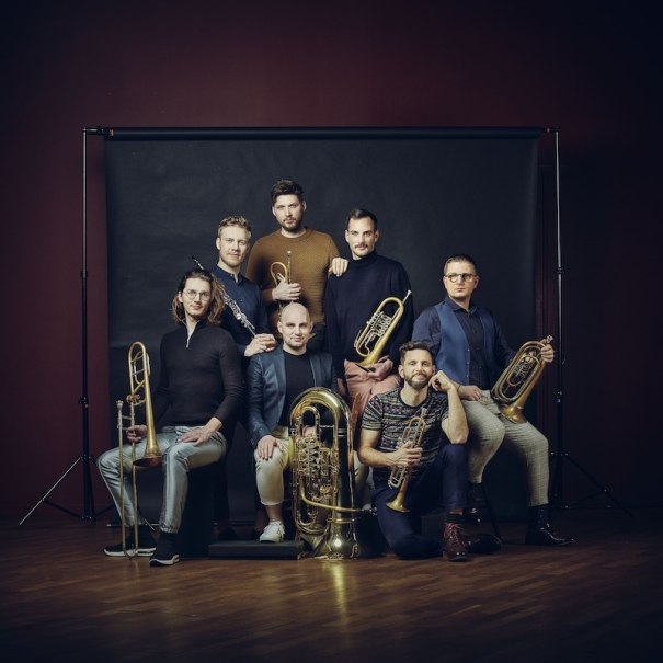 Sieben Männer mit Blasinstrumenten posieren vor einem dunklen Hintergrund. Sie tragen lässige, moderne Kleidung und blicken in die Kamera., © Stadtverwaltung Vaihingen an der Enz