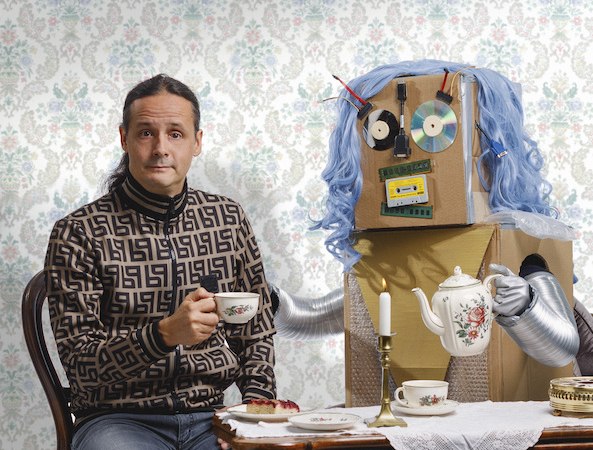 Ein Mann sitzt mit einem Roboter aus Pappe an einem Tisch, trinkt Tee und isst Kuchen. Der Roboter hat blaue Haare und eine Teekanne., © Dieselstrasse Kulturzentrum e.V.