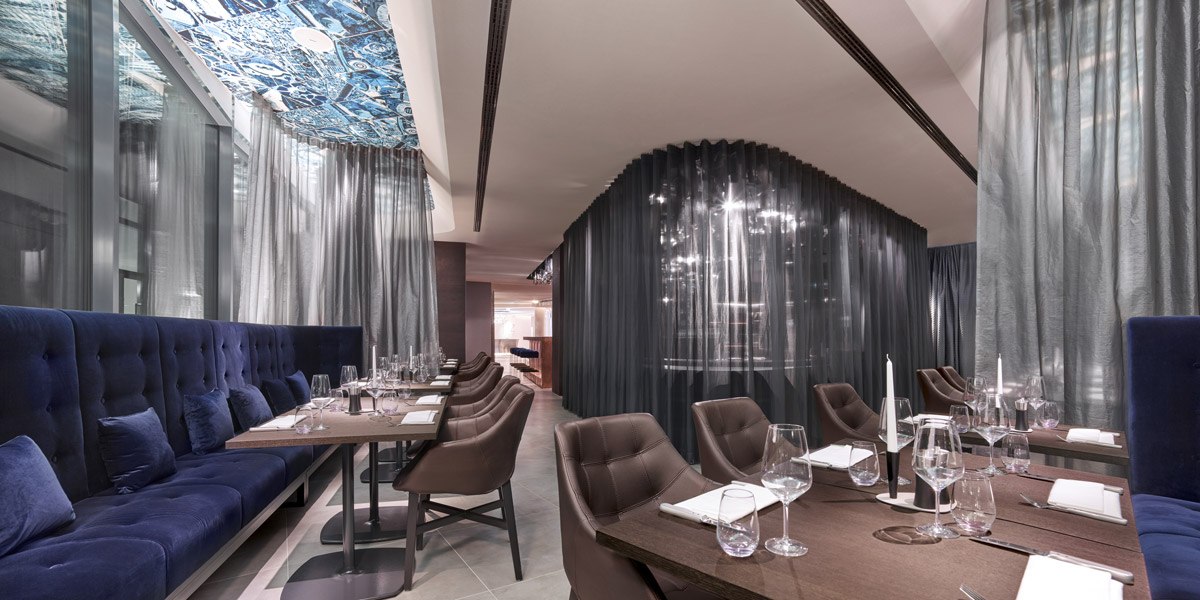 Elegantes Restaurant mit blauen Sitzbänken, gedeckten Tischen und modernen Vorhängen., © Jaz Hotel Stuttgart