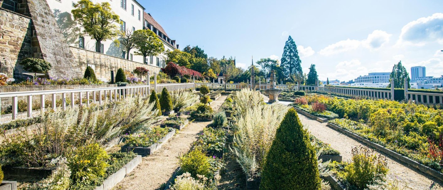 Der Pomeranzengarten in Leonberg zeigt gepflegte Beete und einen zentralen Brunnen, umgeben von historischen Gebäuden und Bäumen unter blauem Himmel., © Stuttgart-Marketing GmbH, Sarah Schmid Der Pomeranzengarten in Leonberg zeigt gepflegte Beete und einen zentralen Brunnen, umgeben von historischen Gebäuden und Bäumen unter blauem Himmel., © Stuttgart-Marketing GmbH, Sarah Schmid