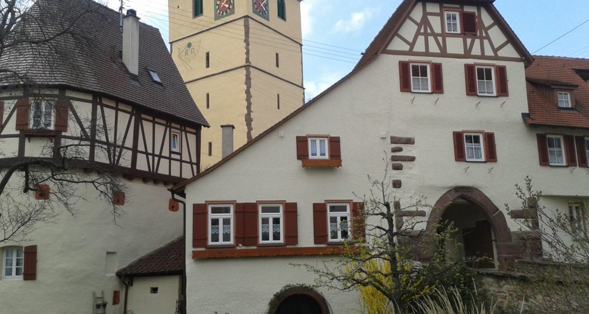 Fachwerkhäuser mit roten Fensterläden vor einem Kirchturm mit Uhr in Merklingen. Der Himmel ist leicht bewölkt., © Natur.Nah. Schönbuch & Heckengäu Fachwerkhäuser mit roten Fensterläden vor einem Kirchturm mit Uhr in Merklingen. Der Himmel ist leicht bewölkt., © Natur.Nah. Schönbuch & Heckengäu