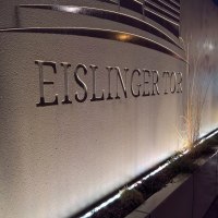 Beleuchtete Steinwand mit der Aufschrift 'Eislinger Tor' und dekorativen Linien. Pflanzen am Boden entlang der Wand., © Hotel Eislinger Tor