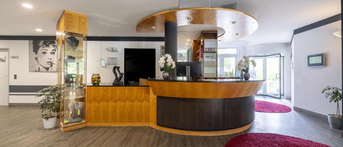 Moderner Empfangsbereich mit Holztheke, Orchideen und einem Bild an der Wand. Rote Teppiche und Glastüren im Hintergrund., © Plaza INN Stuttgart-Filderstadt Moderner Empfangsbereich mit Holztheke, Orchideen und einem Bild an der Wand. Rote Teppiche und Glastüren im Hintergrund., © Plaza INN Stuttgart-Filderstadt