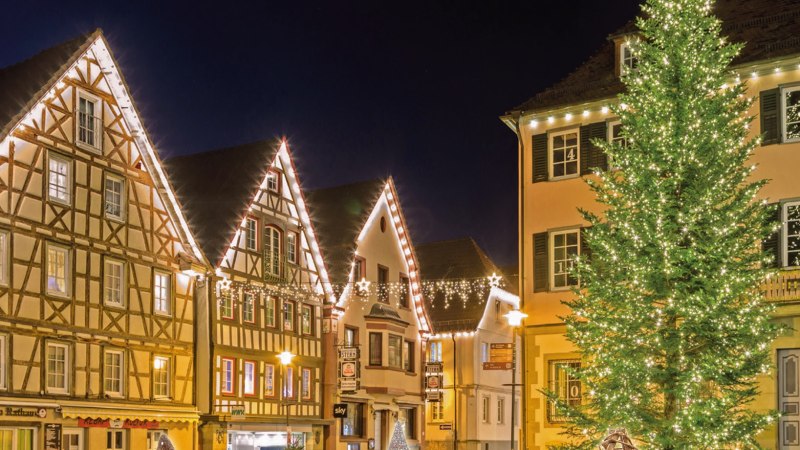 Beleuchtete Fachwerkhäuser und ein großer, geschmückter Weihnachtsbaum bei Nacht auf dem Murrhardter Weihnachtsmarkt., © Stadt Murrhardt