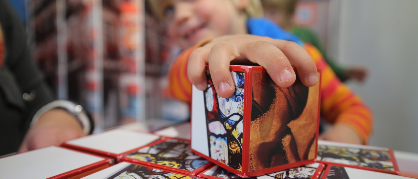 Ein Kind spielt mit bunten Würfeln in der Entdeckerwelt Bad Urach. Der Fokus liegt auf der Hand des Kindes, das einen Würfel hält., © Bad Urach Tourismus