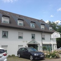 Das Aparthotel Wangener Landhaus mit grauem Dach und weißen Wänden. Vor dem Gebäude sind Autos geparkt. Ein Schild zeigt den Hotelnamen., © Aparthotel Wangener Landhaus