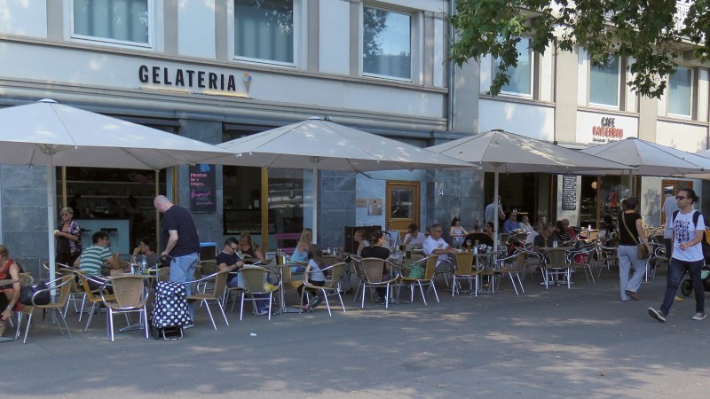 Menschen sitzen unter Sonnenschirmen vor der Gelateria Kaiserbau am Marienplatz. Einige Passanten gehen vorbei., © Stuttgart-Marketing GmbH Menschen sitzen unter Sonnenschirmen vor der Gelateria Kaiserbau am Marienplatz. Einige Passanten gehen vorbei., © Stuttgart-Marketing GmbH