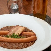 Linseneintopf mit Würstchen und Speck in einem weißen Teller, daneben eine Schüssel Spätzle auf einem Holztisch., © Stuttgart-Marketing GmbH