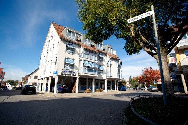 Das AKZENT Hotel Torgauer Hof an einer Straßenecke mit blauen Markisen und einem Baum im Vordergrund., © AKZENT Hotel Torgauer Hof