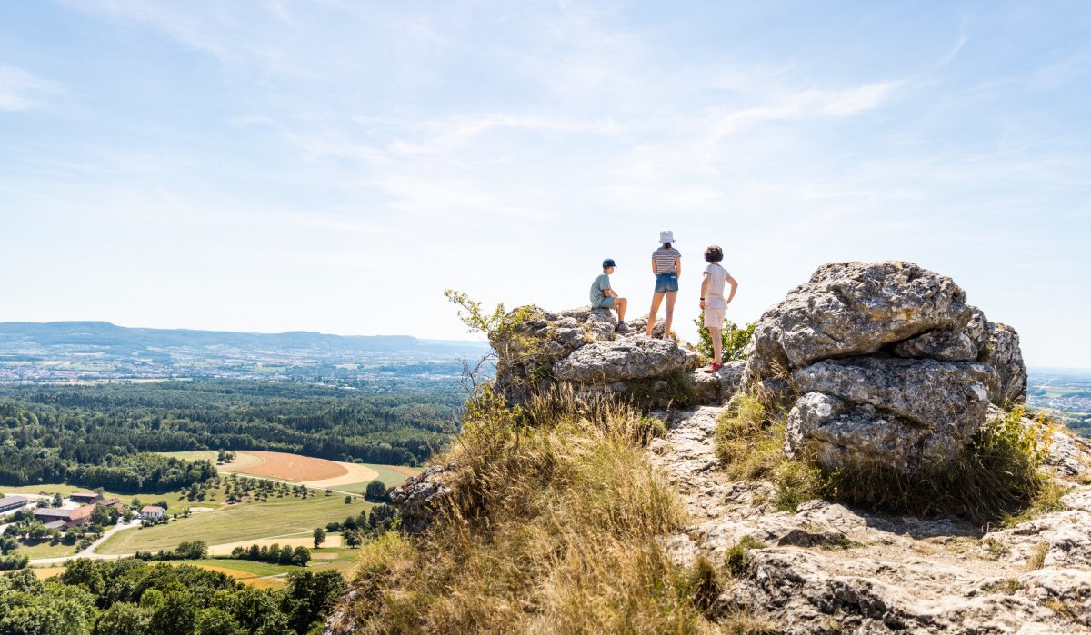 Drei Personen stehen auf einem Felsen und genießen die Aussicht über eine weite Landschaft mit Feldern und Wäldern unter einem klaren Himmel., © Landkreis Göppingen