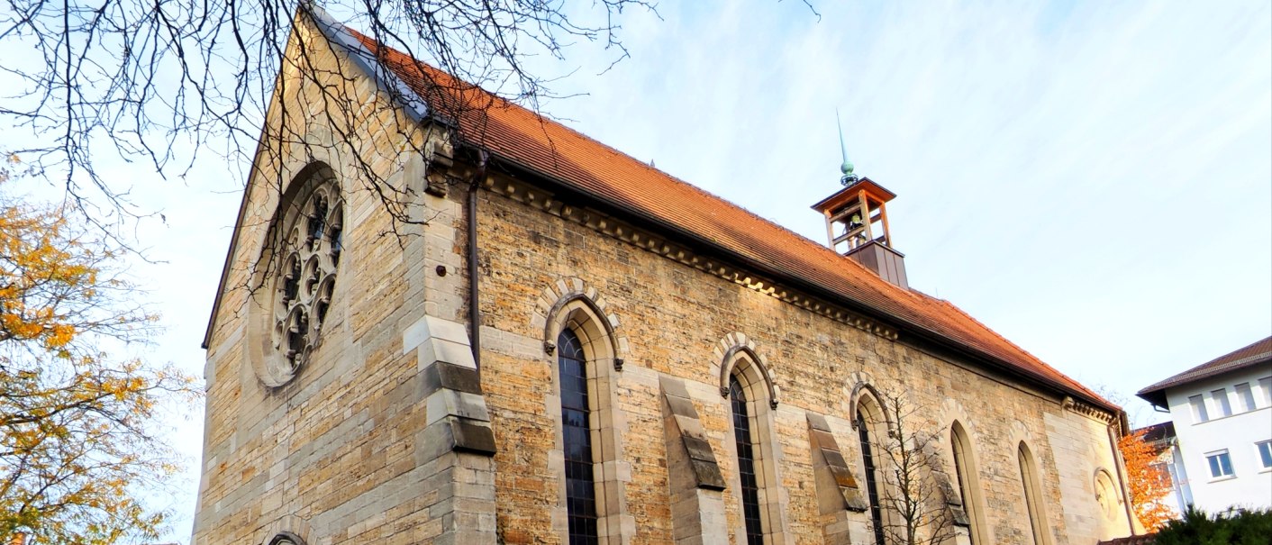 Steinkirche mit rotem Satteldach, Rundfenster und kleinem Glockenturm, von kahlen &Auml;sten und Herbstb&auml;umen umrahmt., &copy; St. Katharina Stuttgart