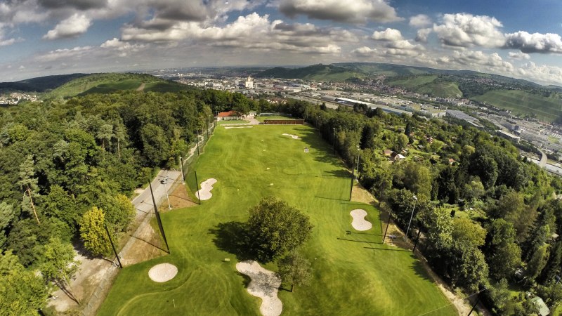 Luftaufnahme eines Golfplatzes in Stuttgart, umgeben von Bäumen und Hügeln, mit der Stadt im Hintergrund unter einem bewölkten Himmel., © GolfKultur Stuttgart