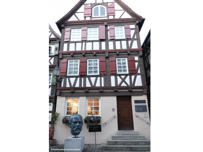 Fachwerkhaus in Schorndorf mit einer B&uuml;ste von Gottlieb Daimler vor dem Eingang. Das Geb&auml;ude hat rote Fensterl&auml;den und eine Treppe f&uuml;hrt zur T&uuml;r., &copy; Eigenbetrieb Tourismus und Citymanagement Schorndorf