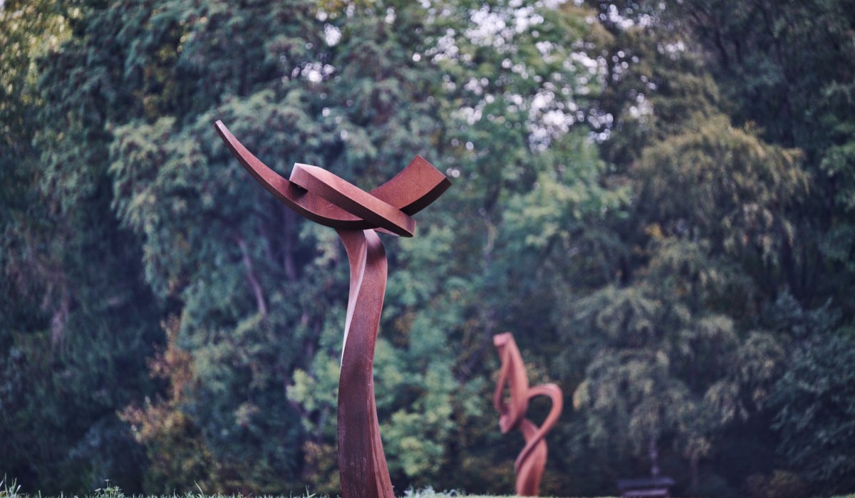 Abstrakte Metallskulpturen in einem Park, umgeben von &uuml;ppigem Gr&uuml;n. Die Skulpturen haben geschwungene Formen und stehen auf einer Wiese., &copy; Natur.Nah. Sch&ouml;nbuch & Heckeng&auml;u