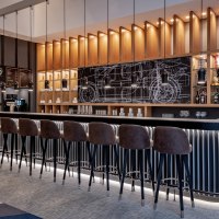 Moderne Bar mit hohen Stühlen, beleuchteten Regalen und einer Tafel mit technischen Zeichnungen im Hintergrund., © copyright by Kilian Blees Moderne Bar mit hohen Stühlen, beleuchteten Regalen und einer Tafel mit technischen Zeichnungen im Hintergrund., © copyright by Kilian Blees