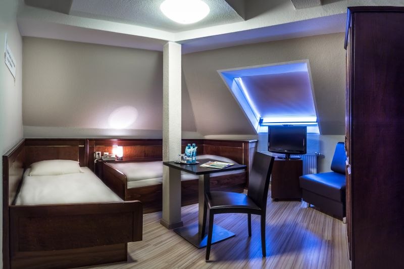 Zweibettzimmer mit zwei Einzelbetten, Tisch, Stuhl und Fernseher unter einer Dachschräge. Modern eingerichtet mit Holzmöbeln und Dachfenster., © TOMAS