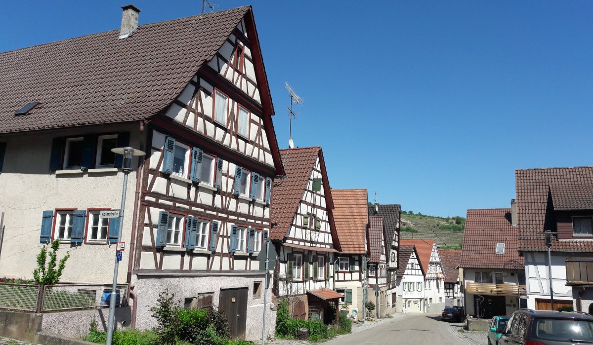 Fachwerkhäuser in Rosswag unter klarem, blauem Himmel. Die Straße ist gesäumt von geparkten Autos und traditionellen Gebäuden., © Land der 1000 Hügel - Kraichgau-Stromberg