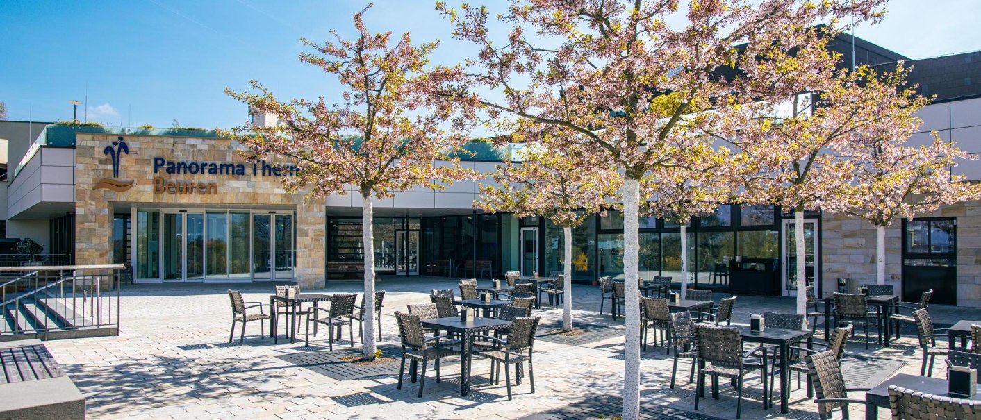 Eingangsbereich der Panorama Therme Beuren mit blühenden Bäumen und leeren Sitzplätzen im Freien. Die Sonne scheint an einem klaren Tag., © Stuttgart-Marketing GmbH, Sarah Schmid Eingangsbereich der Panorama Therme Beuren mit blühenden Bäumen und leeren Sitzplätzen im Freien. Die Sonne scheint an einem klaren Tag., © Stuttgart-Marketing GmbH, Sarah Schmid