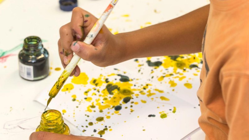 Ein Kind malt mit einem Pinsel und gelber Farbe auf Papier. Die H&auml;nde sind farbig verschmiert, und es gibt Farbspritzer auf dem Papier., &copy; Ludwigsburg Museum