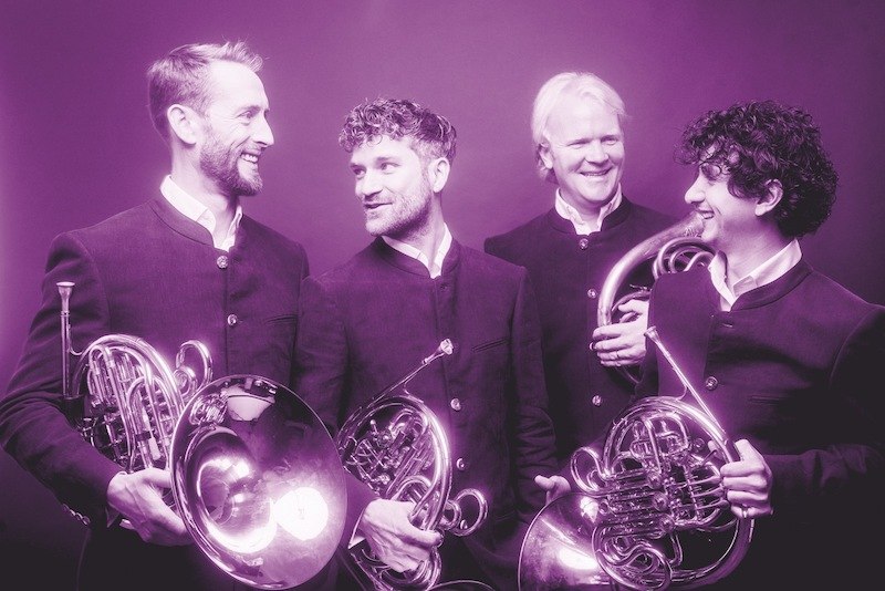 Vier M&auml;nner in dunklen Anz&uuml;gen halten H&ouml;rner und l&auml;cheln sich gegenseitig an. Das Bild ist in einem lila Farbton gehalten., &copy; Kulturstiftung Hohenlohe