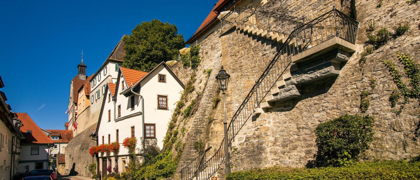 Die Altstadt von Besigheim zeigt malerische Fachwerkhäuser und eine steinerne Treppe an einer alten Stadtmauer unter klarem, blauem Himmel., © Stuttgart-Marketing GmbH, Sarah Schmid