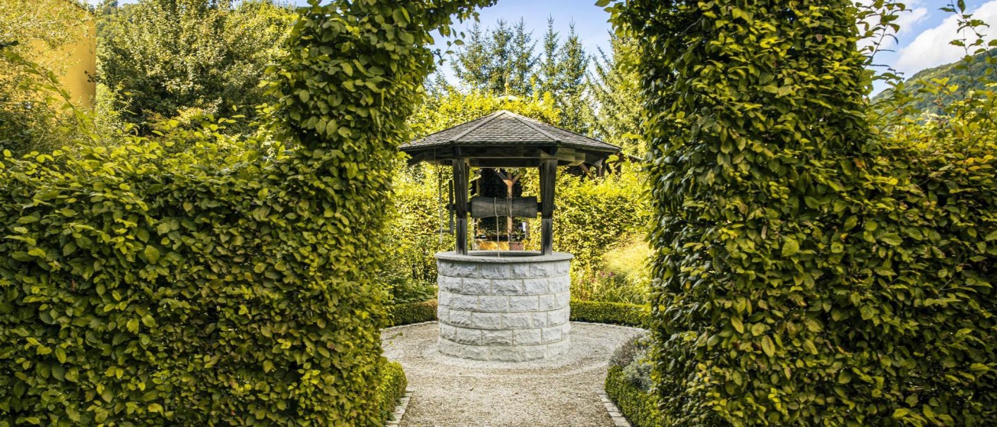 Ein steinerner Brunnen mit Holzdach steht in einem üppigen Garten, umgeben von grünen Hecken und Bäumen., © Stuttgart-Marketing GmbH, Sarah Schmid Ein steinerner Brunnen mit Holzdach steht in einem üppigen Garten, umgeben von grünen Hecken und Bäumen., © Stuttgart-Marketing GmbH, Sarah Schmid