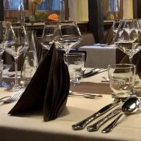 Elegante Tischdekoration in einem Restaurant mit Weingläsern, Besteck und gefalteten Servietten auf weißen Tischdecken., © Wirtshaus zom Schiller Fellbach