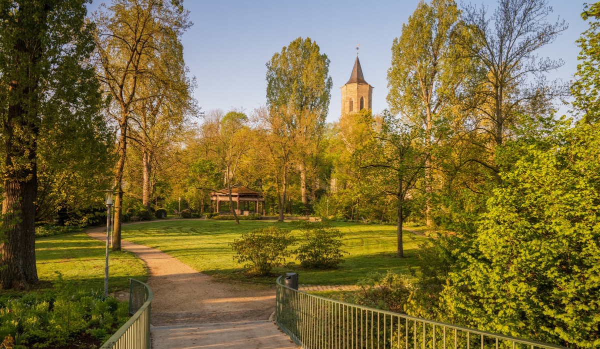 Ein grüner Park mit einem Weg, der zu einem Pavillon führt. Im Hintergrund ist ein Kirchturm zu sehen, umgeben von Bäumen im Sonnenlicht., © Remstal Tourismus e.V.