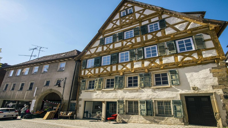 Außenansicht eines historischen Fachwerkhauses in Waiblingen, umgeben von anderen Gebäuden, bei strahlend blauem Himmel., © SMG, Sarah Schmid