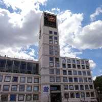 Ein modernes Geb&auml;ude mit einem hohen Uhrturm und vielen Fenstern. Der Himmel ist blau mit einigen Wolken., &copy; Fei Shiyu