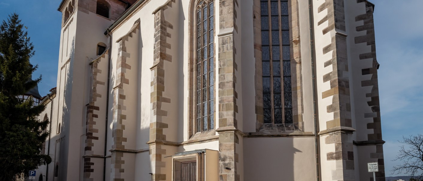 Die Stiftskirche Backnang mit gotischen Fenstern und rotem Dach, umgeben von einem gepflasterten Platz, unter einem klaren blauen Himmel., © René Straube
