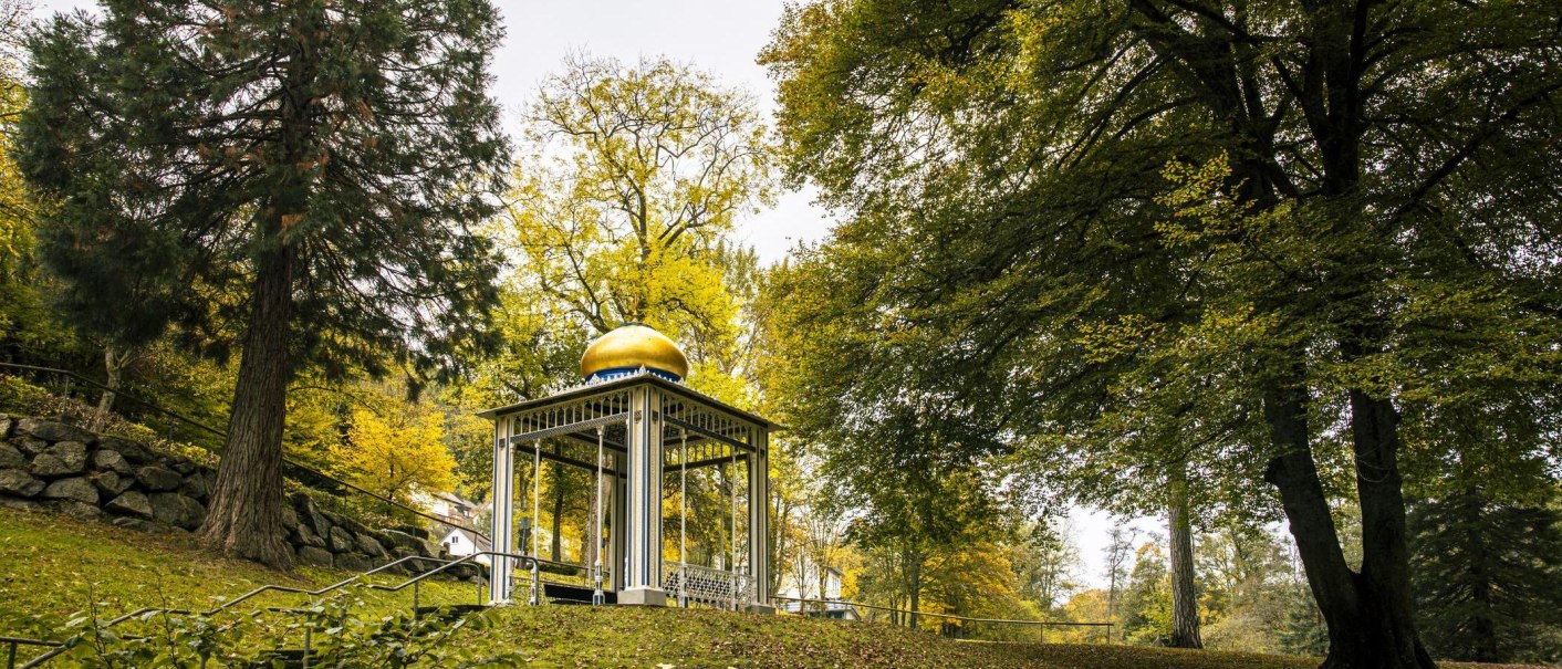 Ein Pavillon mit goldener Kuppel steht im Kurpark von Bad Wildbad, umgeben von herbstlich gef&auml;rbten B&auml;umen und einem gr&uuml;nen Rasen., &copy; SMG, Sarah Schmid
