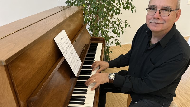 Ein Mann spielt an einem Holzklavier, l&auml;chelt und schaut in die Kamera. Im Hintergrund steht eine Pflanze., &copy; Klaus Leonhardt