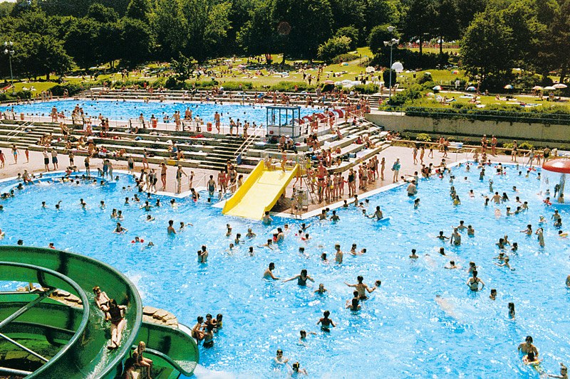 Ein belebtes Freibad mit vielen Menschen im Wasser und auf der Liegewiese. Eine gelbe Rutsche und eine grüne Wasserrutsche sind sichtbar., © Stadt Wendlindgen am Neckar Ein belebtes Freibad mit vielen Menschen im Wasser und auf der Liegewiese. Eine gelbe Rutsche und eine grüne Wasserrutsche sind sichtbar., © Stadt Wendlindgen am Neckar