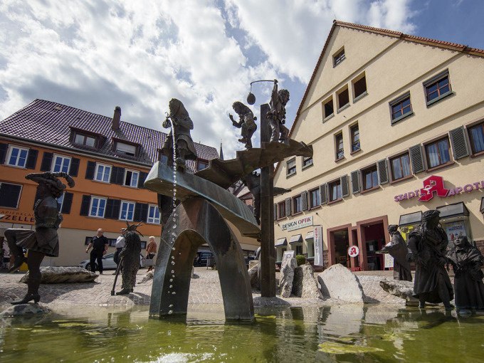 Ein Brunnen mit skurrilen Figuren in einer Altstadt. Die Figuren stellen verschiedene Szenen dar und sind um einen zentralen Wasserlauf gruppiert., &copy; Stadtverwaltung Weil der Stadt