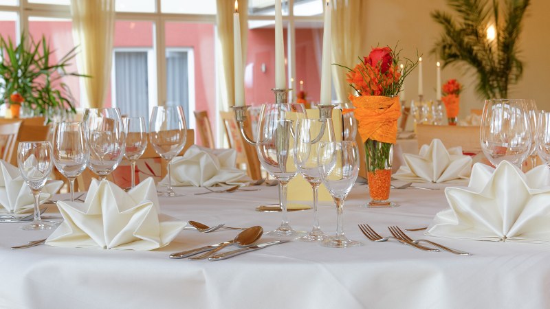 Eleganter Tisch im Hotel-Restaurant mit weißen Servietten, Gläsern und Kerzen. Blumendekoration in Orange. Große Fenster im Hintergrund., © Hotel-Restaurant "Talblick" Eleganter Tisch im Hotel-Restaurant mit weißen Servietten, Gläsern und Kerzen. Blumendekoration in Orange. Große Fenster im Hintergrund., © Hotel-Restaurant "Talblick"