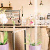 Ein stilvolles Caf&eacute; mit einer modernen Theke, Barhockern und Orchideen im Vordergrund. Im Hintergrund sind Gl&auml;ser und Flaschen zu sehen., &copy; cMagnolia