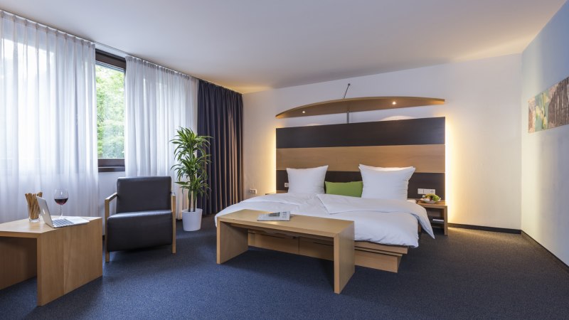 Modernes Hotelzimmer mit Doppelbett, Sessel, Tisch, Laptop und Glas Wein. Fenster mit Vorhängen, Pflanze und stilvolle Beleuchtung., © Hotel Berlin aZIS Hotel BetriebsGmbH Modernes Hotelzimmer mit Doppelbett, Sessel, Tisch, Laptop und Glas Wein. Fenster mit Vorhängen, Pflanze und stilvolle Beleuchtung., © Hotel Berlin aZIS Hotel BetriebsGmbH