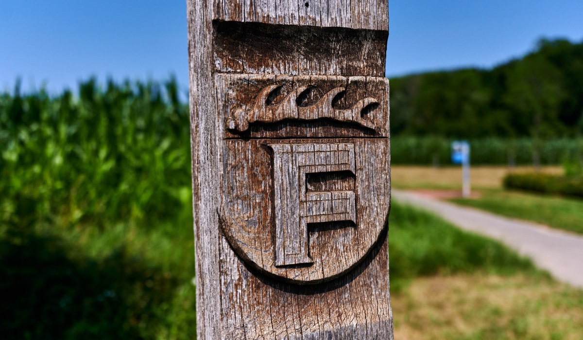 Holzpfosten mit geschnitztem Wappen und Buchstabe F, im Hintergrund ein Weg und grüne Landschaft., © Kraichgau-Stromberg Tourismus e.V. Holzpfosten mit geschnitztem Wappen und Buchstabe F, im Hintergrund ein Weg und grüne Landschaft., © Kraichgau-Stromberg Tourismus e.V.